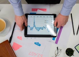 Top view of a professional analyzing financial data on a tablet at a desk.